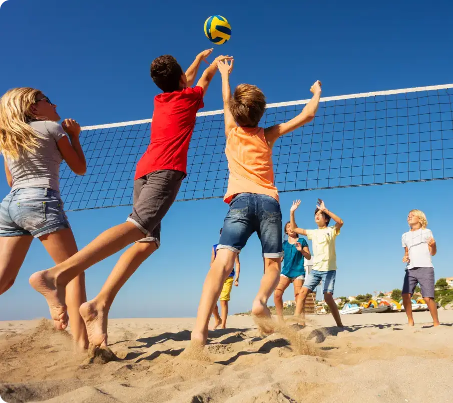 Children playing beach volleyball on a sunny day energetically jump and reach for the ball near the net. The clear blue sky witnesses their boundless joy, a perfect break from understanding technology and nurturing teen mental health in such vibrant sand-filled fun.