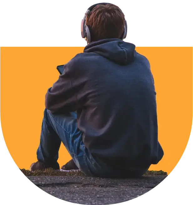 A person, possibly pondering the effects of porn addiction, sits on the ground, wearing headphones and a hoodie, facing away. The backdrop is a solid orange color.